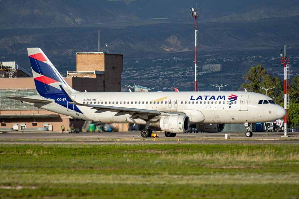 LATAM Airbus A320 taxiing on runway with mountainous backdrop.