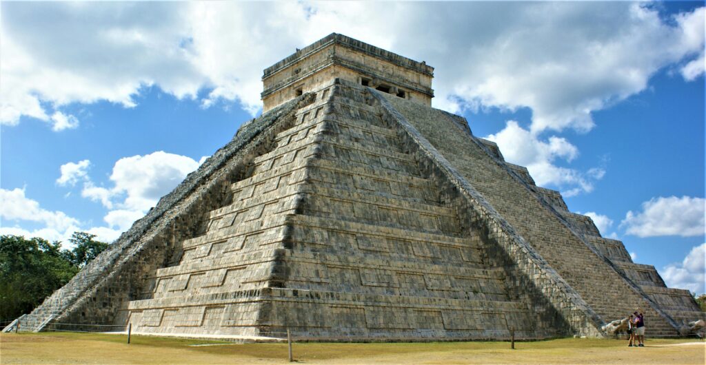 Capture of the iconic Chichen Itza pyramid against a bright blue sky with white clouds in Mexico.