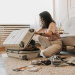 A woman packing her suitcase in a stylish living room, surrounded by clothes and travel accessories.