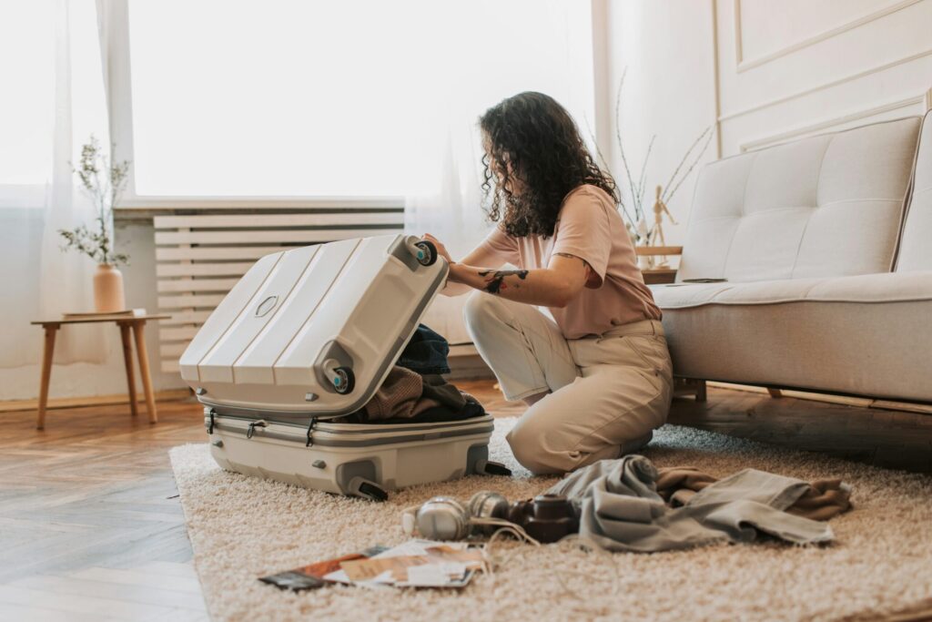 A woman packing her suitcase in a stylish living room, surrounded by clothes and travel accessories.