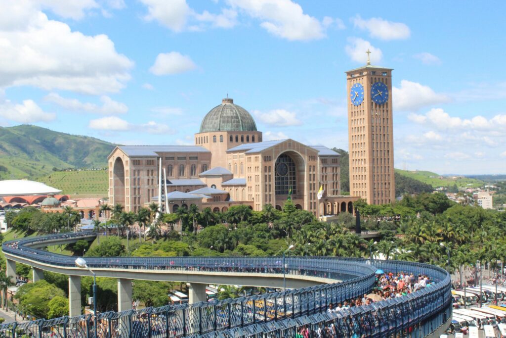 A sweeping view of the Basilica of Nossa Senhora Aparecida surrounded by lush greenery and hills.