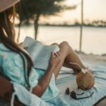 Woman enjoys a peaceful sunset reading session on Zanzibar beach with a coconut drink nearby.