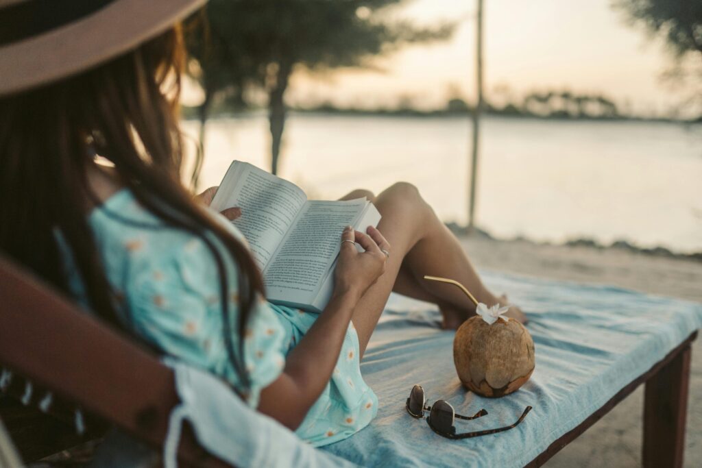 Woman enjoys a peaceful sunset reading session on Zanzibar beach with a coconut drink nearby.