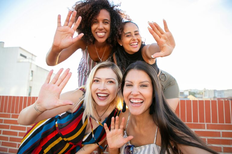 A group of diverse friends enjoying a sunny rooftop hangout, waving and smiling joyfully.